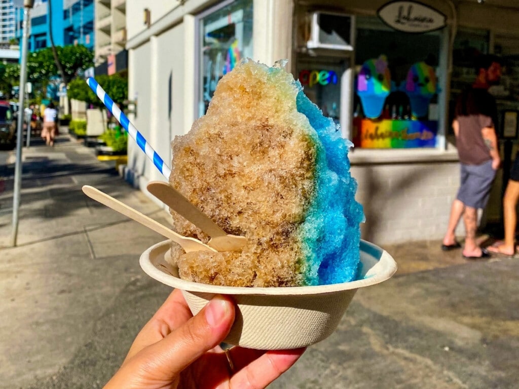 Hand holding out colourful Shave ice in front of the Lahaina Shave Ice stall.