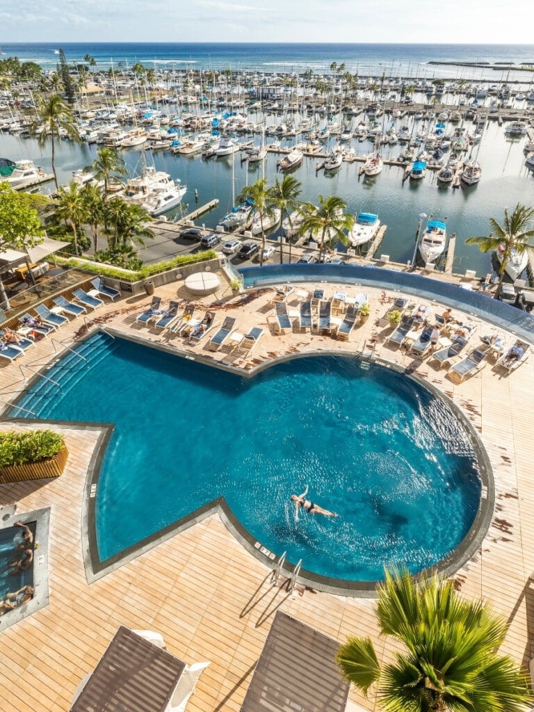 Prince Waikiki Hotel’s luxurious pools, overlooking the marina filled with sailboats and yachts. With sun loungers, a relaxing hot tub, and tropical palm trees,