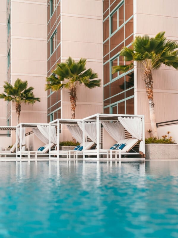 An image of Prince Waikiki's pool area with luxurious white cabanas and palm trees lining the edge of the pool.