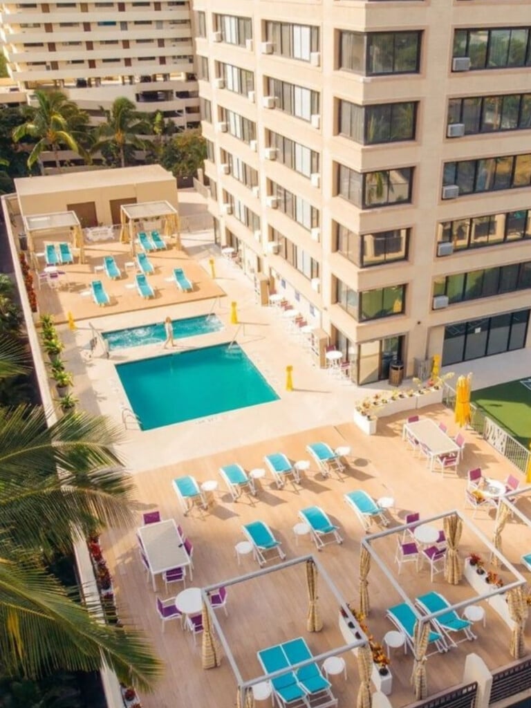 The rooftop pool area of the Holiday Inn Express Waikiki, featuring bright lounge chairs, tables, and private cabanas. Set against the backdrop of the hotel, the area has a modern vibe.