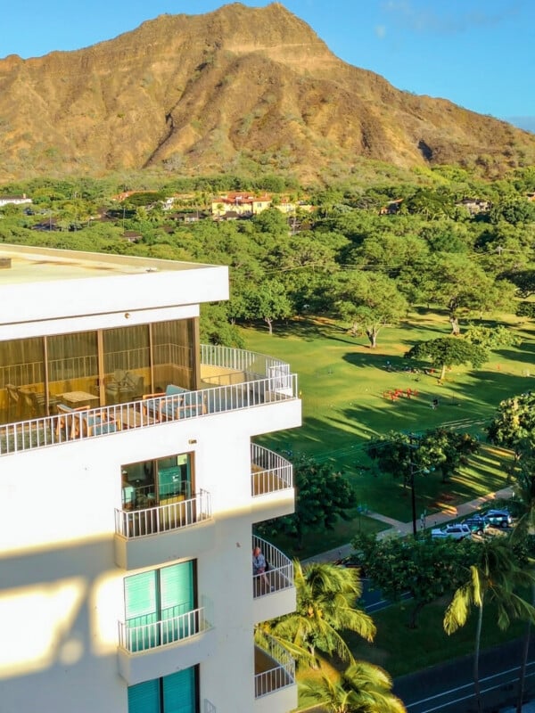 A stunning view of the Lotus Honolulu hotel with private balconies, set against the lush greenery and the towering backdrop of Diamond Head Crater in Hawaii.