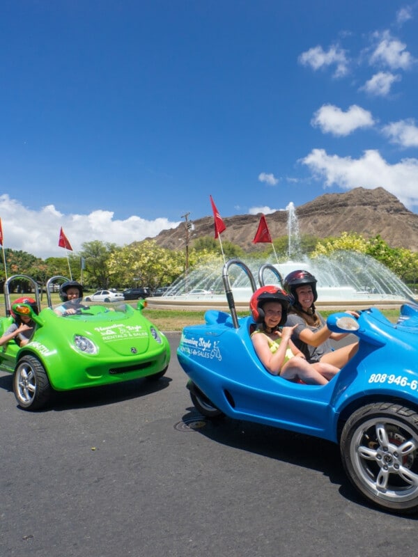 One blue and one green Scoot Coupe driving past the fountain and Diamond head