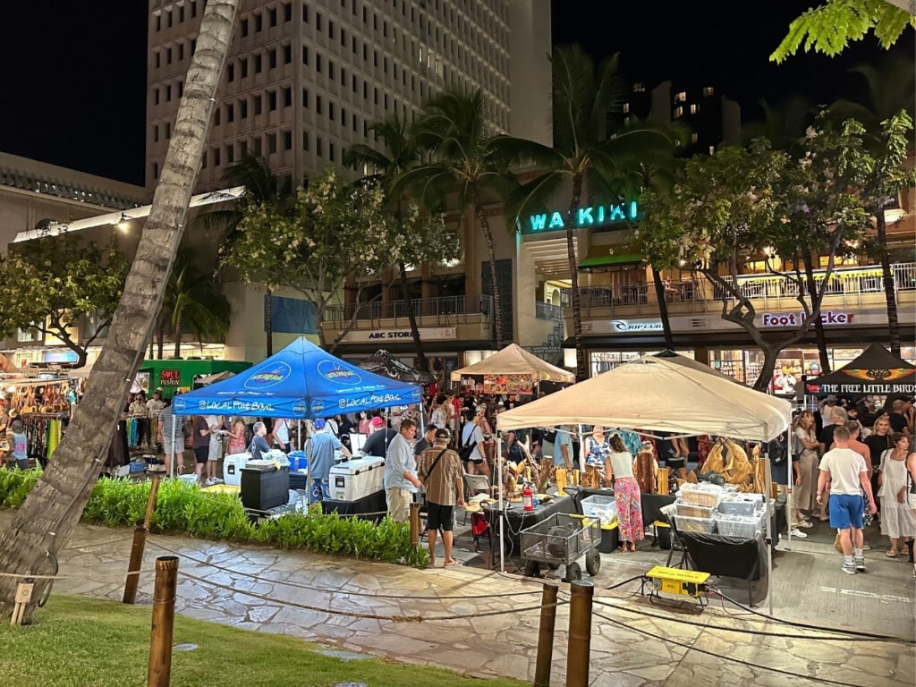 A busy block party/street festival happening at night on Kalākaua Avenue in Waikīkī.