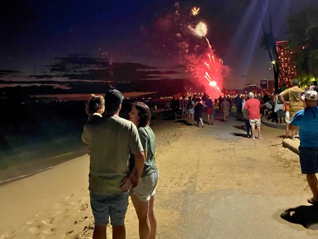 The Waikīkī Friday Night Fireworks going off at the Hilton Hawaiian Village with a couple and a child watching them in happiness.