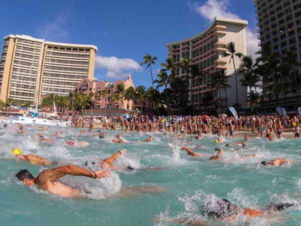 Hundreds of swimmers race  in the Duke’s Waikiki Ocean Mile Swim during the Duke Kahanamoku Ocean Festival. The event draws large crowds to the beach for swimming, surfing, and other ocean sports, set against the backdrop of iconic Waikiki hotels.