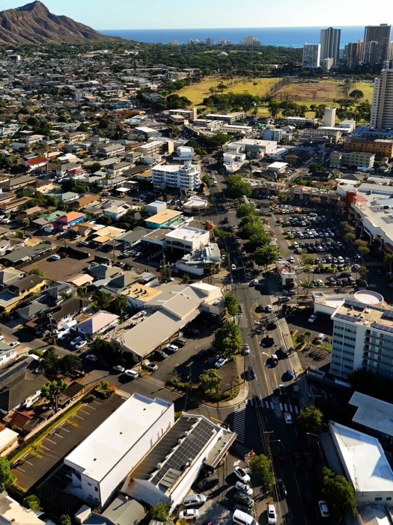 Arial view of Honolulu's Kapahulu neighborhood, showcasing Diamond Head in the background with vibrant urban and residential areas.