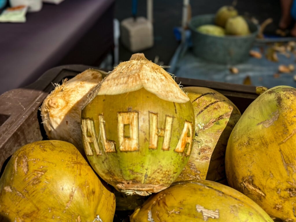 Pile of fresh coconuts with a coconut with the word "ALOHA" carved onto it at Kaka’ako Farmers Market.