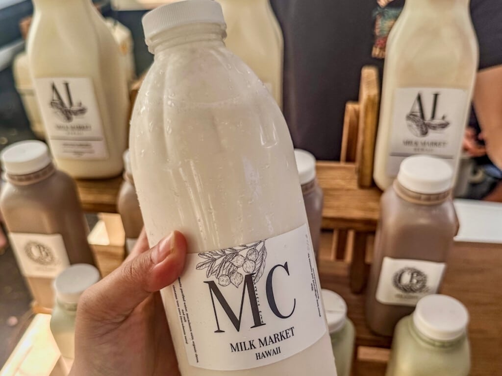 Hand holding a fresh bottle of MC Milk Market Hawaii at Kaka'ako Farmers Market.