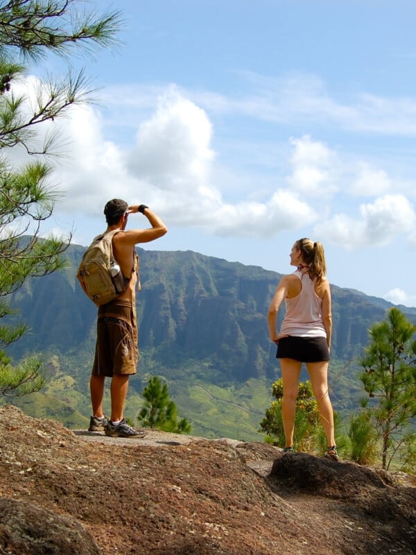 Two hikers on a trail in Hawaiʻi, standing on the top of a mountain.