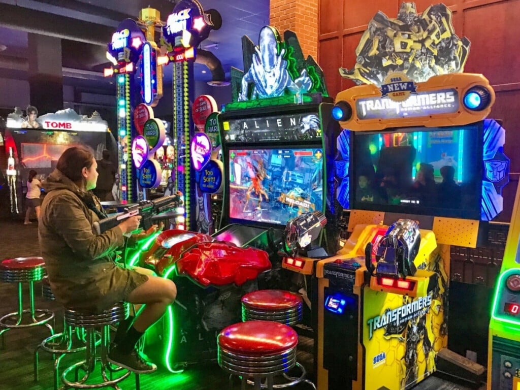 Kelii focused on playing a colorful arcade game, surrounded by flashing lights and vibrant machines at Dave & Buster's Honolulu.