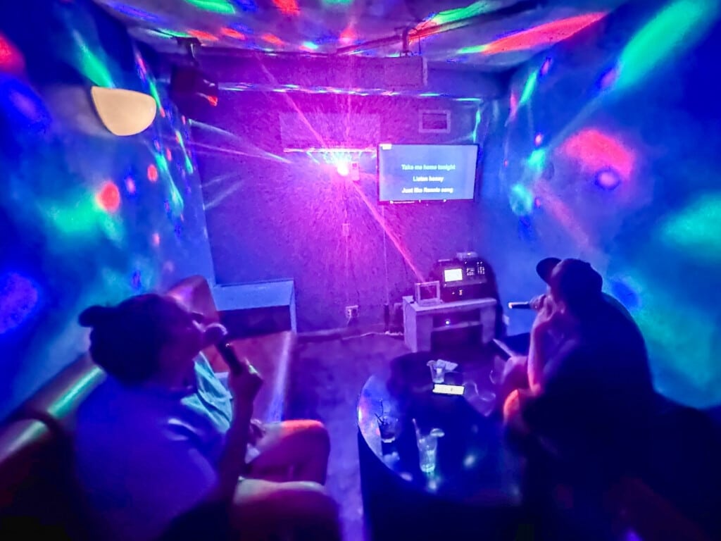 Two friends singing at Karaoke GS Studio Waikiki in a room lit up with disco lights. 