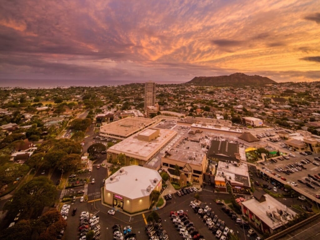 A stunning aerial view of Kahala Mall at sunset, located near Waikiki, highlighting its expansive shopping center. It is surrounded by scenic landscapes.