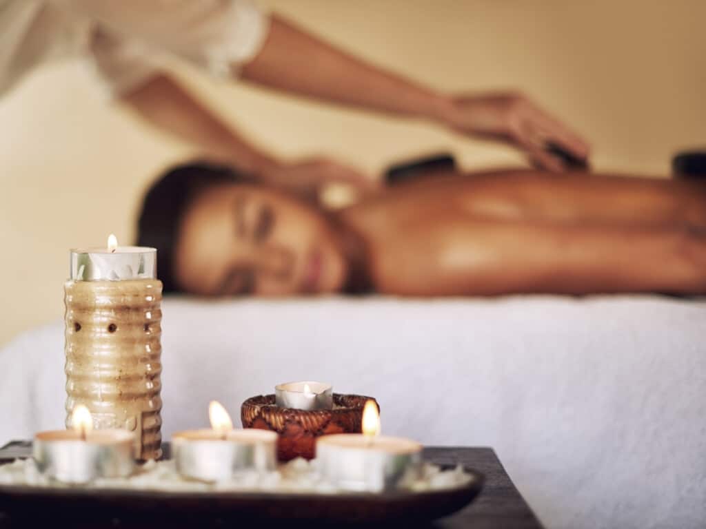 Lady having a Hawaiian lomilomi massage with hot rocks with aroma therapy candles in the foreground.