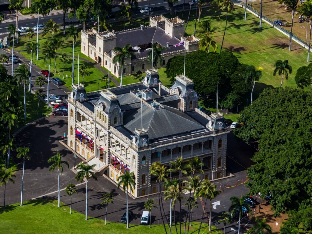 Arial shot of ʻIolani Palace surrounded by palm trees and green grass.
