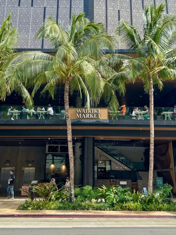 Street view of the exterior of Waikiki Market on Kūhiō Avenue with palm trees in the foreground.