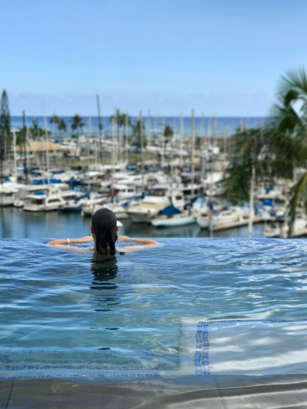 A woman in the infinity edge pool at Prince Waikiki looking out over all the boats docked Ala Wai Boat Harbor.