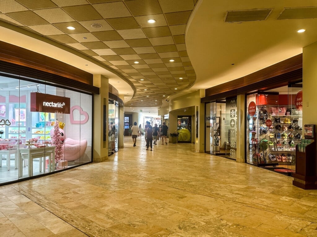 Interior view of Sheraton Waikiki shopping center featuring boutique stores, bright displays and polished walkway.