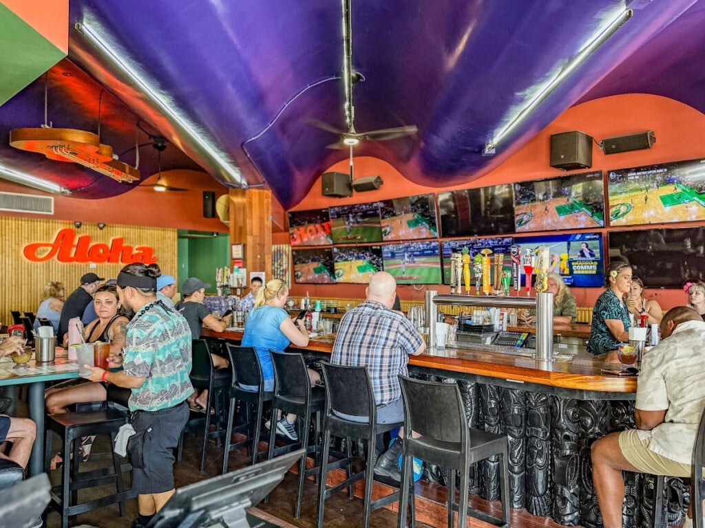 The bar area at Cheeseburger in Paradise with people watching a sports game on the big screen.