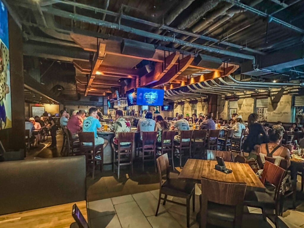 The bar area at Yard House restaurant in Waikiki and people watching a game on the big screen above the bar.