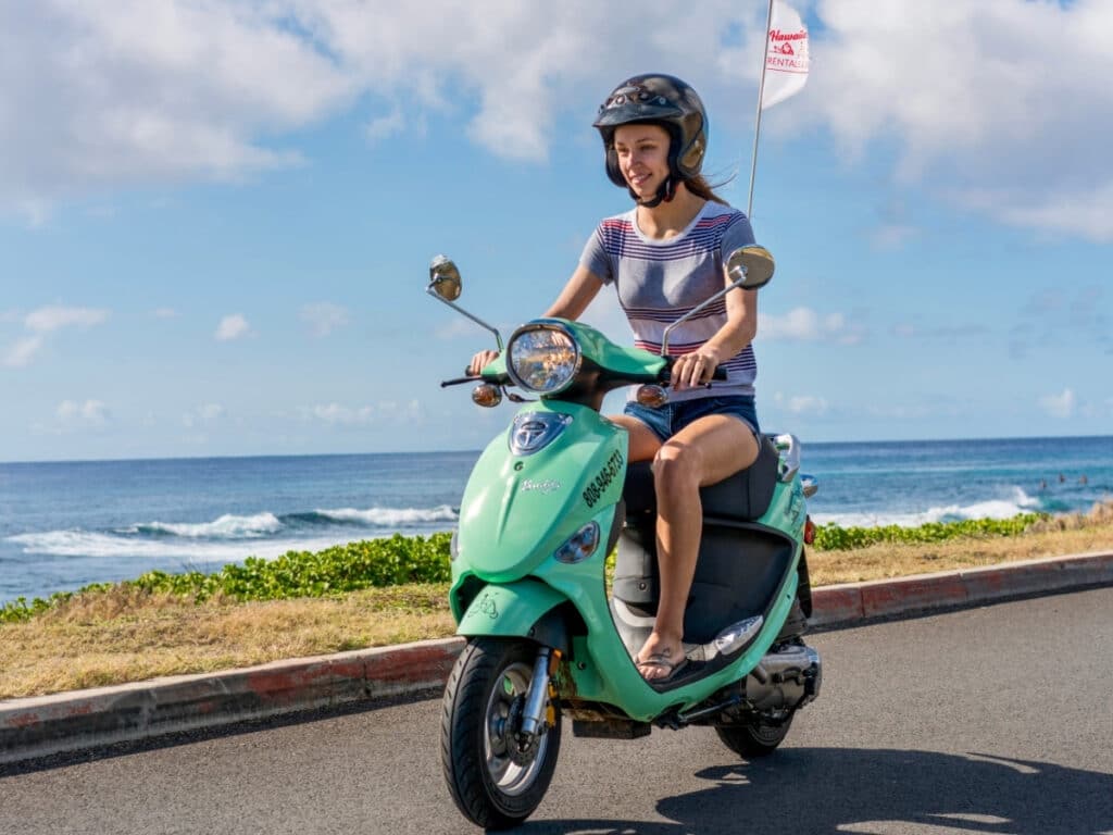 A solo rider on a aqua-blue moped rental from Hawaiian Style Rental, cruising the coastal area of O'ahu, Hawai'i.