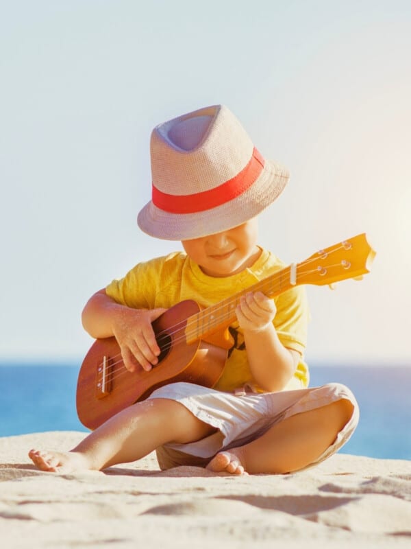 A little boy playing ukulele at sunny sea beach.