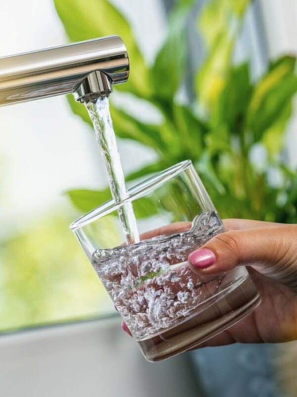 A woman hand holds a glass to fill it with water from tap.