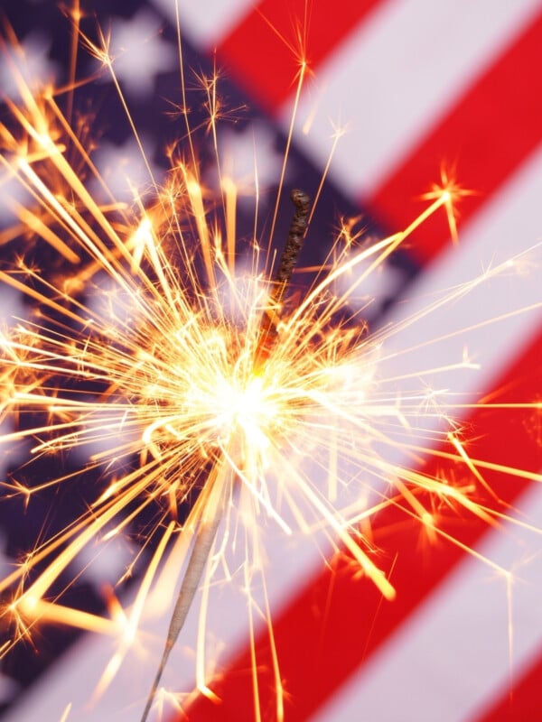 Bright sparkler with an American flag in the background.