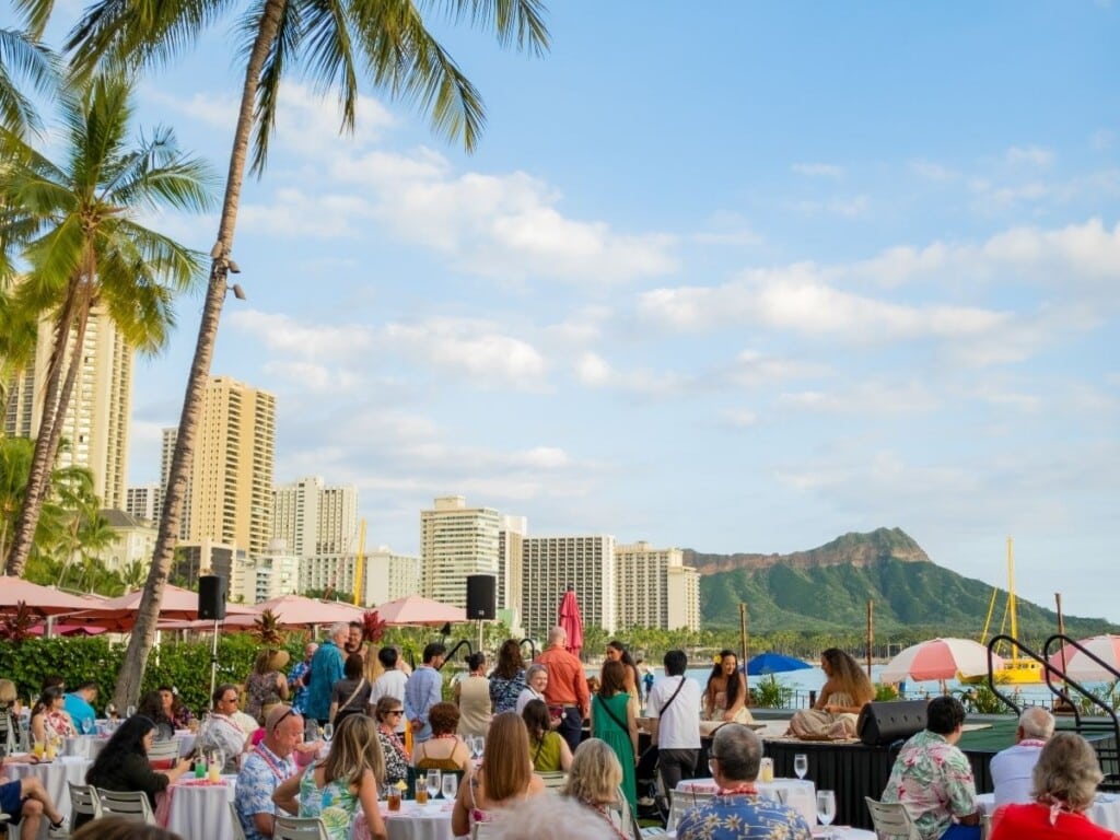 Waikīkī Beach is the star of the show at the Aha‘aina Luau at The Royal Hawaiian, setting a stunning scene. A stage stands with a fence, keeping wandering visitors mostly out of sight.