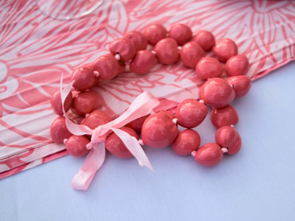 A pink kukui nut lei rests on a table covered with a pink and white tablecloth at the Aha‘aina Luau.