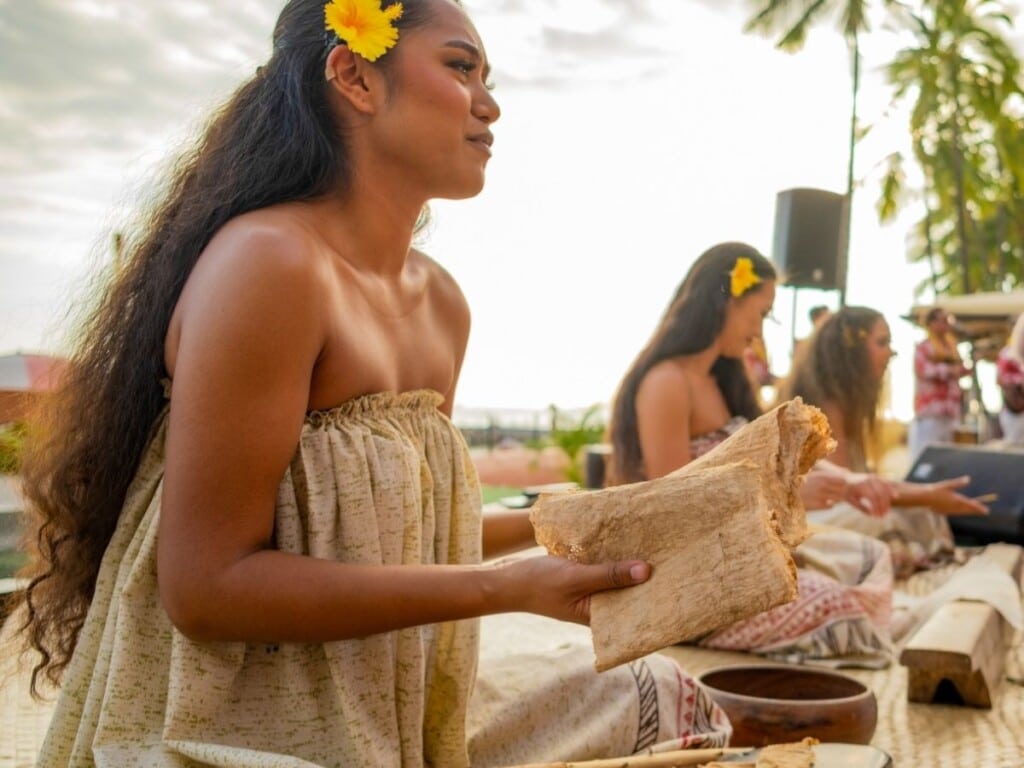 Three dancers sit on stage, demonstrate the six steps involved in this traditional process at ʻAhaʻaina, A Royal Hawaiian Lūʻau.