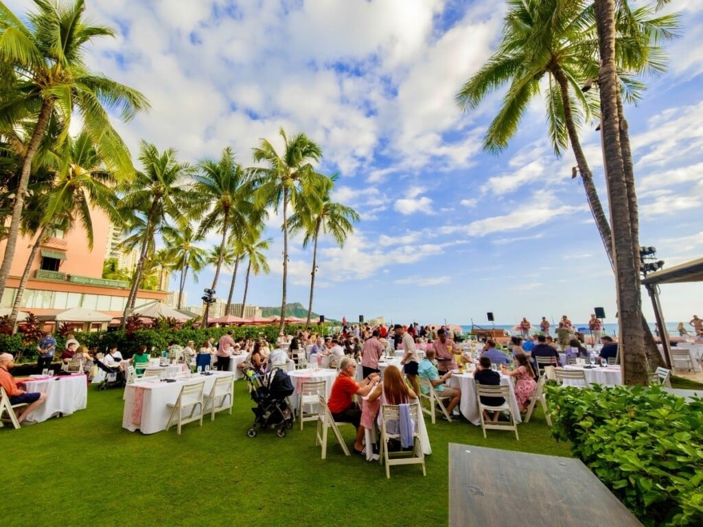 The ʻAhaʻaina, A Royal Hawaiian Lūʻau setting which takes place on the front lawn, of the iconic Royal Hawaiian Hotel. There is a stunning, open view of Waikīkī beach and Diamond Head - a perfect place to watch the sunset.