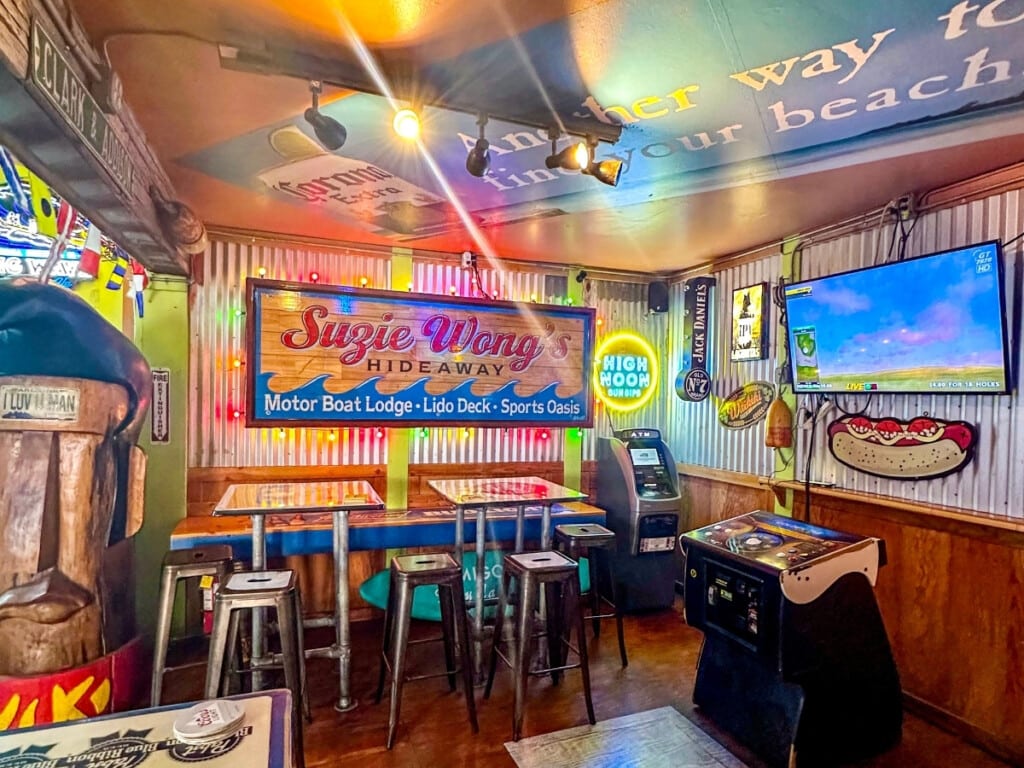 Cozy interior of Suzie Wong’s Hideaway bar in Waikīkī featuring vintage decor, neon signs, arcade games, and high-top seating.