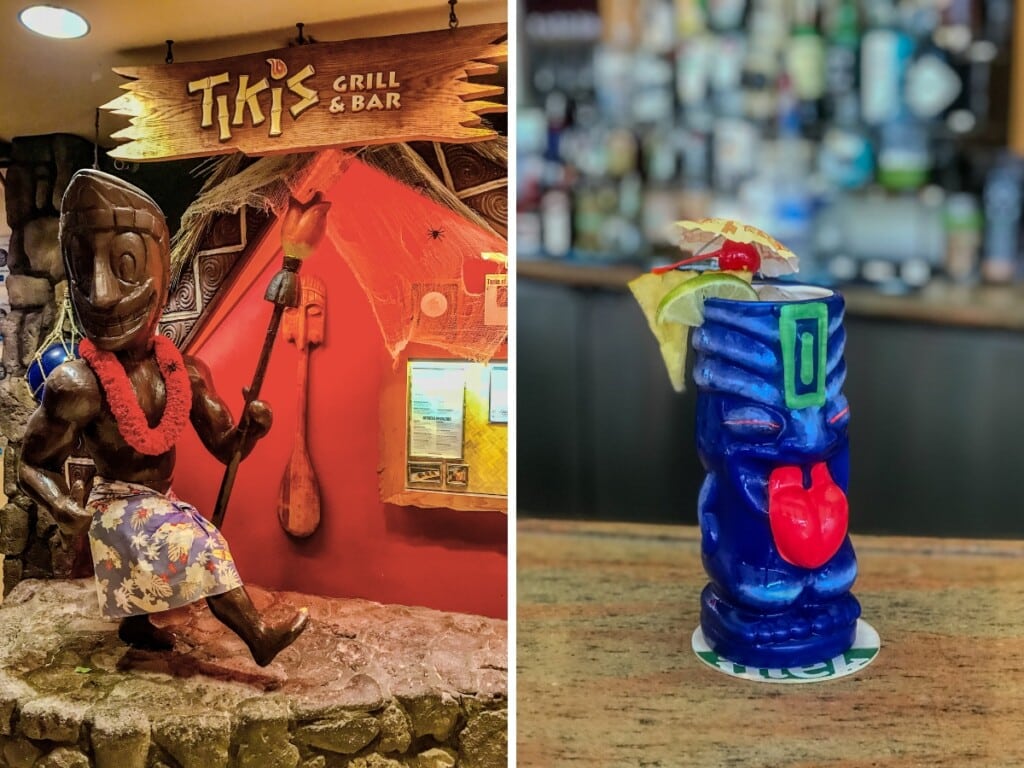 Entrance of Tiki's grill & bar Waikīkī themed entrance with wooden signage and smiling tiki statue that is wearing a red lei. Right; Cocktail served in their special tiki mug.