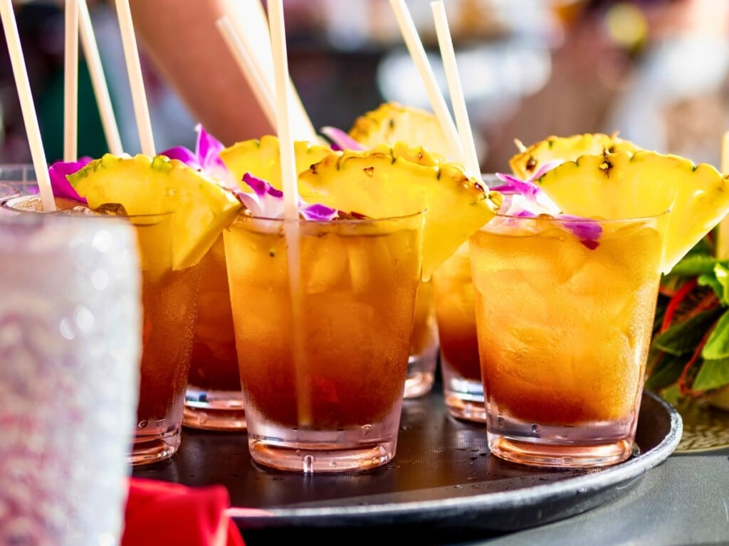 Tray of mai tais garnished with pineapples and colorful purple orchids and cheersing at Pāʻina Waikīkī Luau.