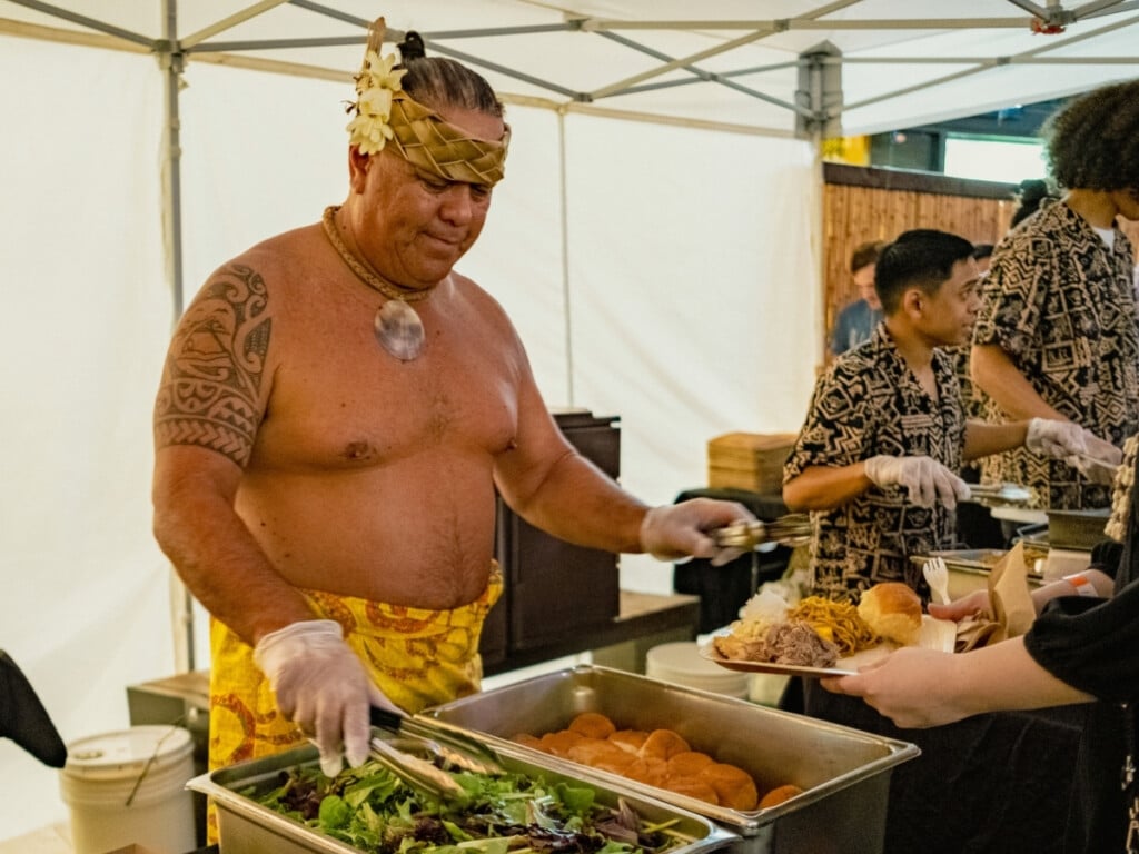 Man dressed in traditional Polynesian clothing serving guests in the buffet at the Queens Waikiki Luau.