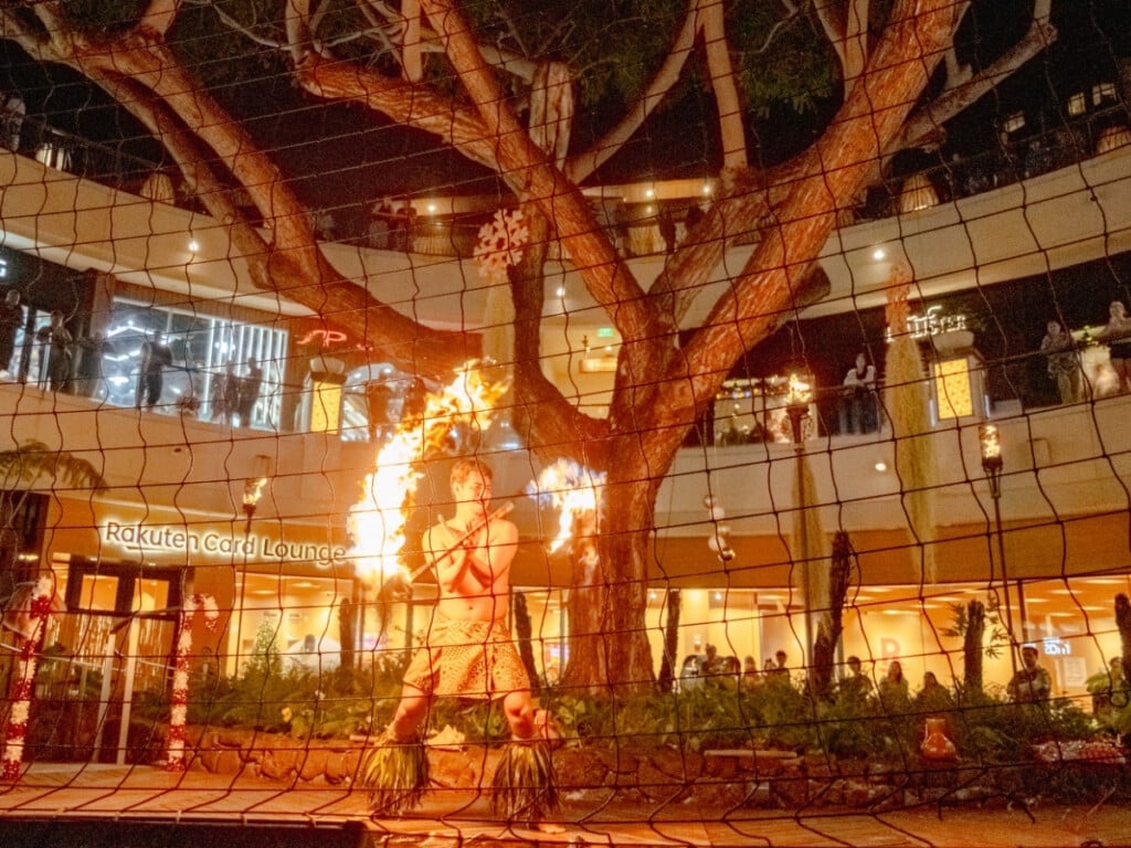 Fire knife dancer behind a safety net twirls firesticks at the Queens Waikiki Luau at the International Market Place in Waikīkī, O‘ahu, Hawaiʻi.