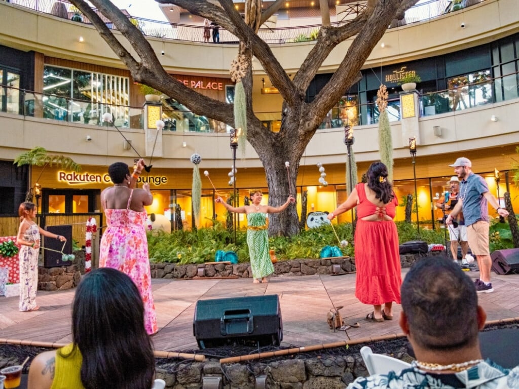 Guests engage in interactive cultural activities and learn how to use authentic Hawaiian dance instruments under the banyan tree of the Queens Waikiki Luau.