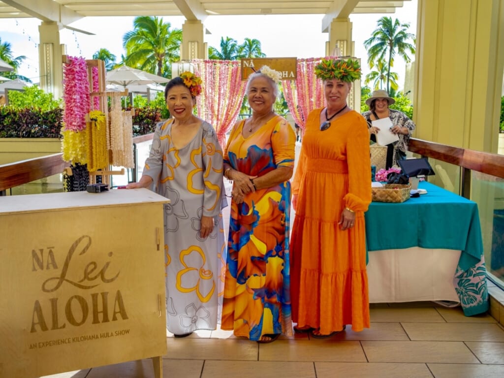Three ladies in bright dresses and big smiles create the perfect welcome at Nā Lei Aloha.