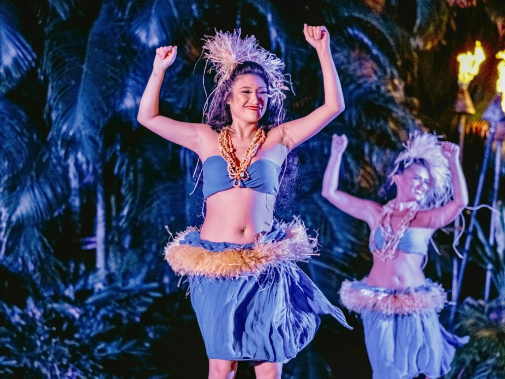 Tahitian dancer performing at Waikiki Starlight Luau adorned in traditional attire with tropical setting an tiki torches in the background.