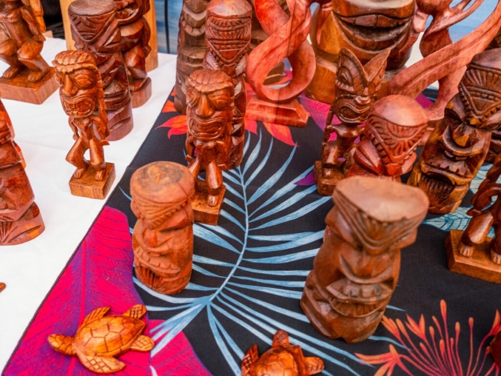 Display of wooden tiki carvings on colorful tropical table cloth at the Waikiki Starlight Luau: Rooftop.