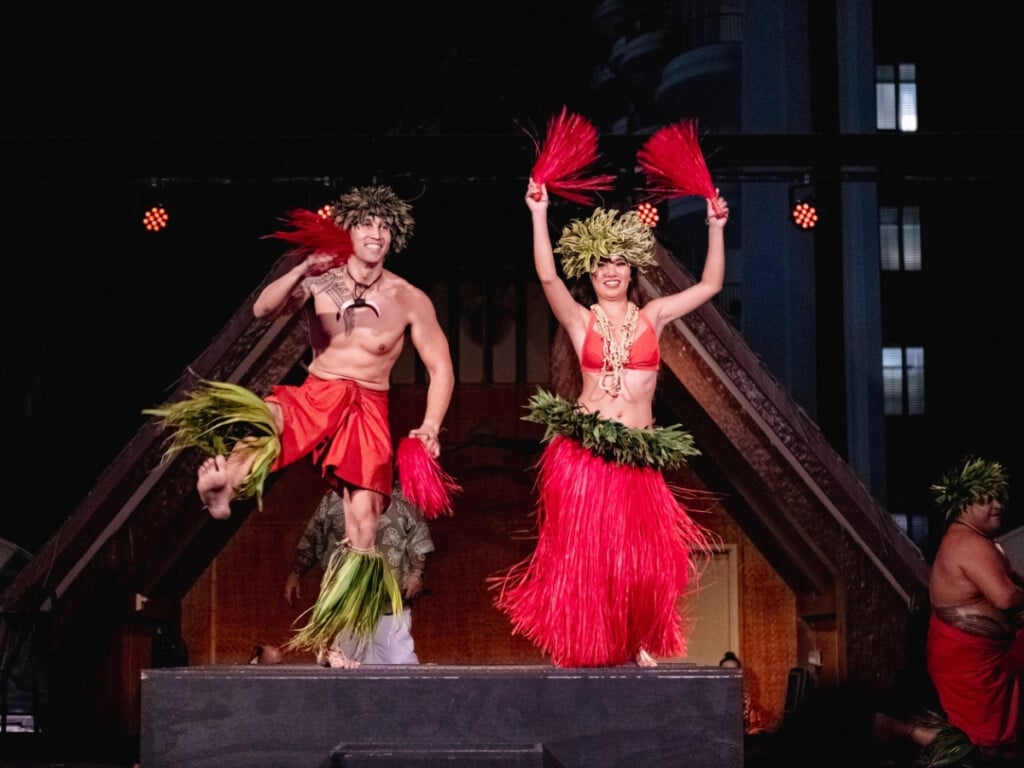 Tahitian dancers in bright red costumes performing at the Waikiki Starlight Luau: Rooftop.