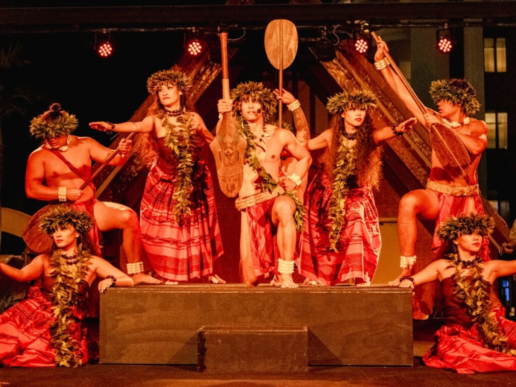 Authentic Hawaiian performance with dancers dressed in traditional red Hawaiian attire with lei and crowns made of tee-leaves at the Waikiki Starlight Luau: Rooftop.