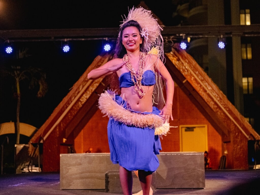 Tahitian dancer performing at Waikiki Starlight Luau: Rooftop adorned in traditional attire on stage.