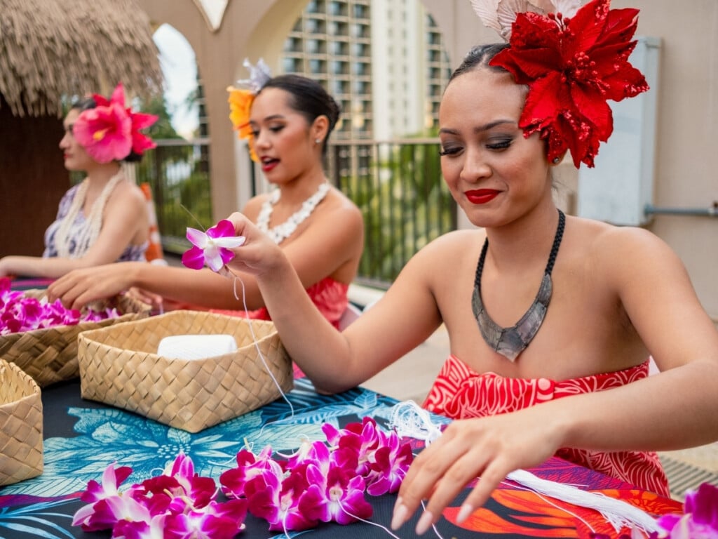 Three ladies making fresh orchid lei bracelets for luau guests at the Waikiki Starlight Luau: Rooftop.