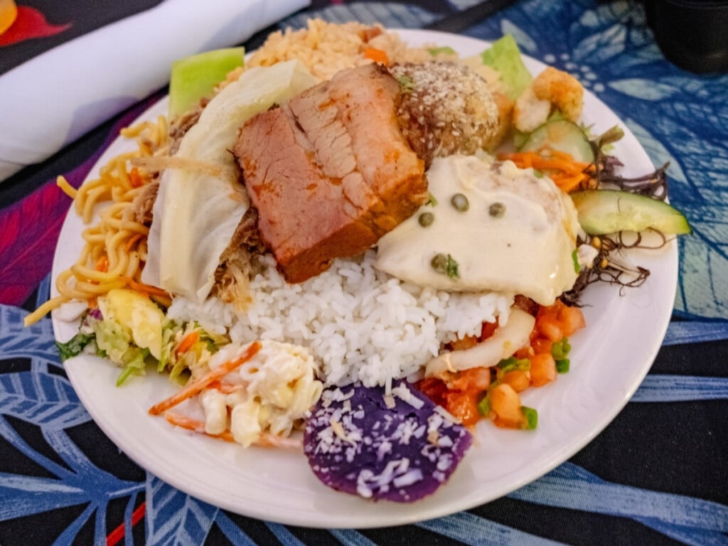 A colorful plate full of food featuring taro, rice, pork and sides from the luau buffet at the Waikiki Starlight Luau: Rooftop.