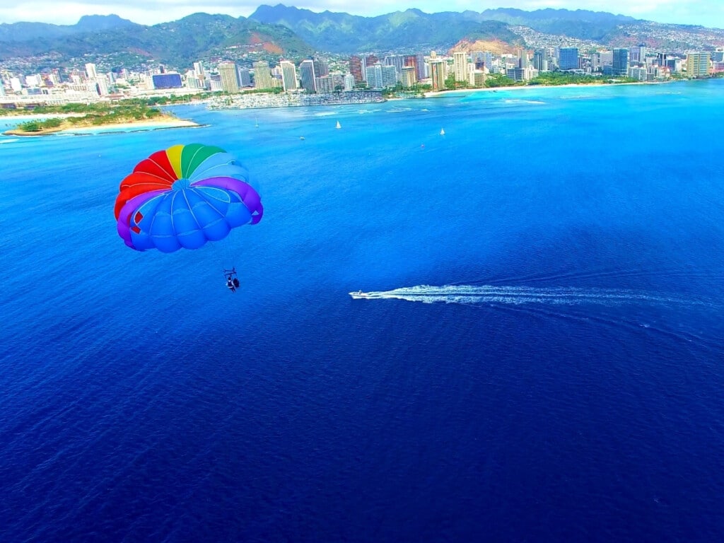 A rainbow parasail sailing off the coast of Waikīkī with a deep blue ocean setting.