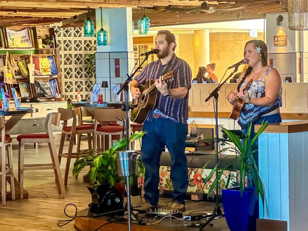 Two musicians performing with guitars at Monkeypod Kitchen in Waikīkī, creating a relaxed and laid-back atmosphere for guests enjoying the live music experience.