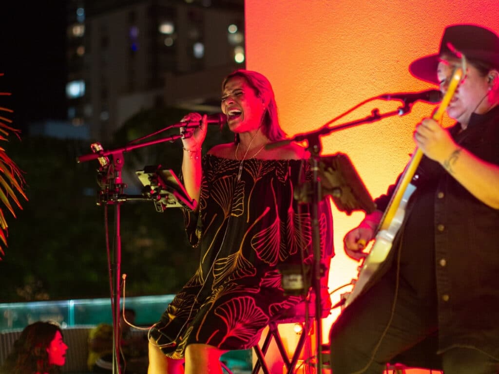 Two people performing live music under orange and red lighting at The Hideout, on the lānai (balcony) at The Laylow hotel.