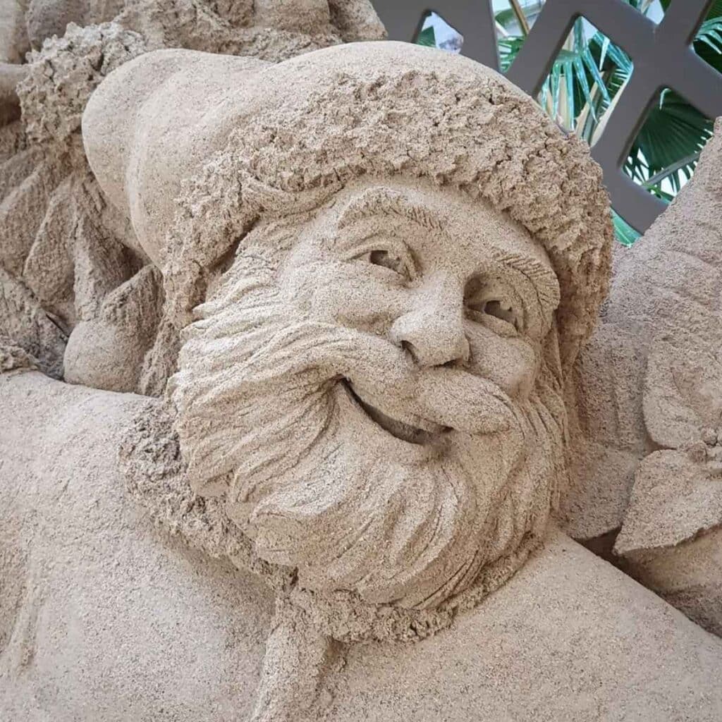 Santa Claus sand sculpture with a detailed beard and Santa hat, created for the Christmas season in Waikīkī.